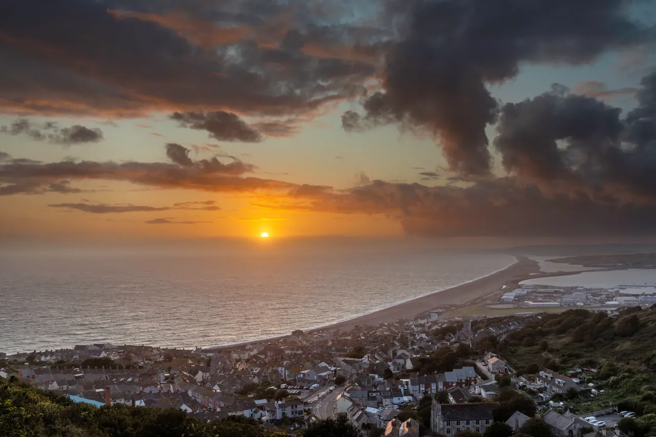Sunset over Fortuneswell on Portland with Chesil Beach curving towards Weymouth, Dorset