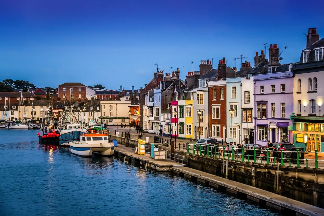 Weymouth harbour at dusk with fishing boats moored below the old quayside houses, Dorset